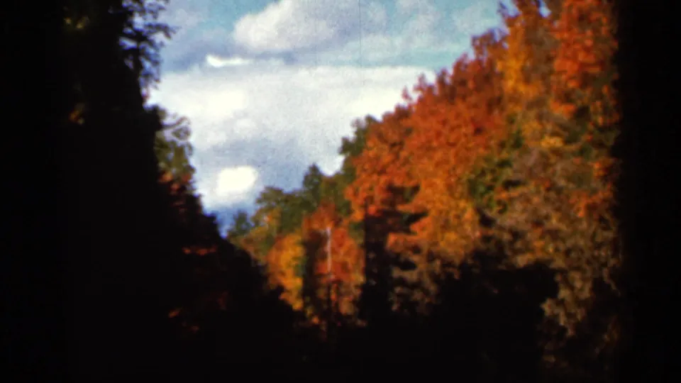 1966 Wauseon, Ohio frame with saturated fall foliage, clouds, and shadowed edges from a handheld 8mm view.