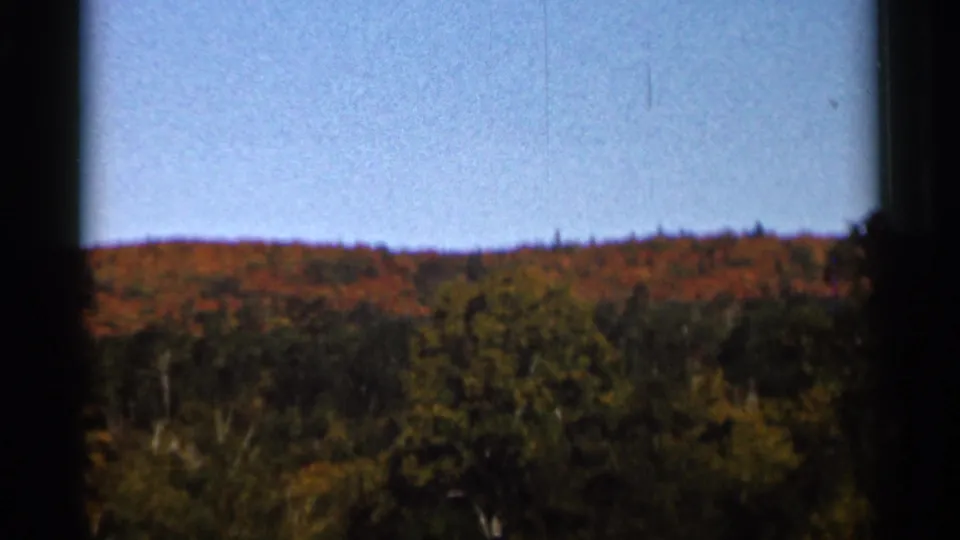 1966 Wauseon, Ohio frame showing a distant autumn wooded slope, low brush, pale blue sky, and dark 8mm frame edges.