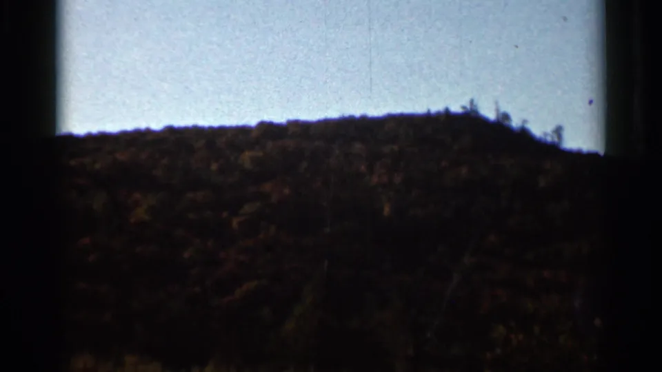 1966 Wauseon, Ohio 8mm frame showing a darker wooded slope with autumn color and a bright blue sky above.