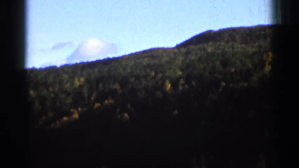 1966 8mm home-movie view of distant wooded hills, partly obscured by dark frame shadows and soft exposure.