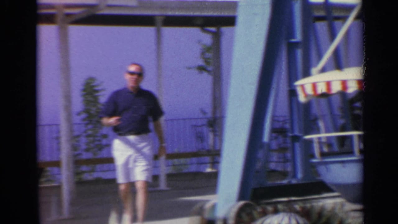 Man walking past a seaside amusement ride with a striped canopy at frame edge.