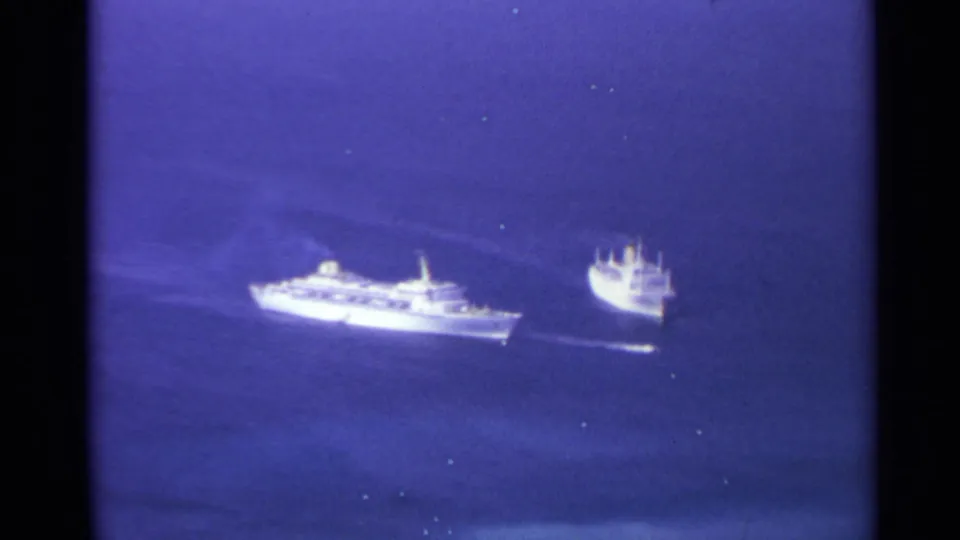 1967 8mm footage frame with two distant white vessels continuing across open sea, both leaving subtle wake lines.
