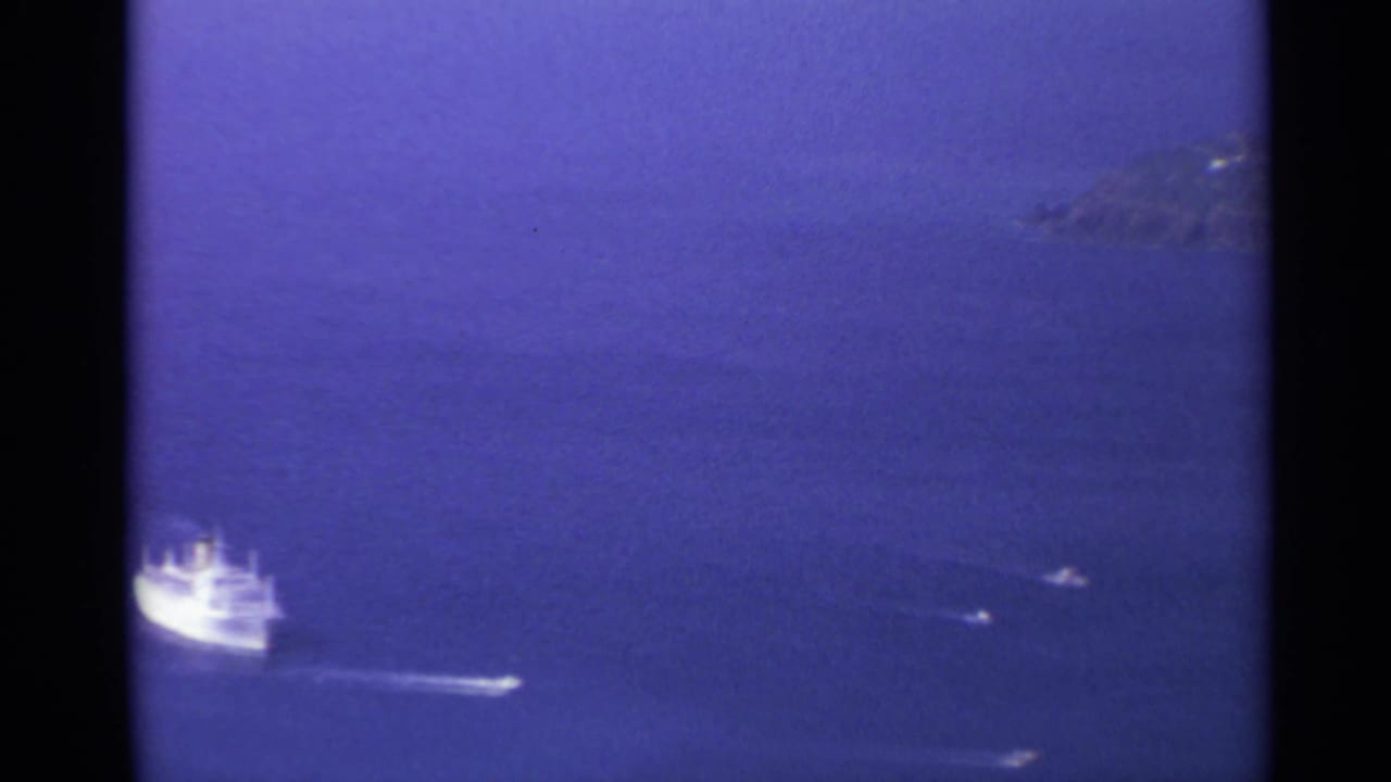 White ship crossing deep blue water near distant rocky islands.
