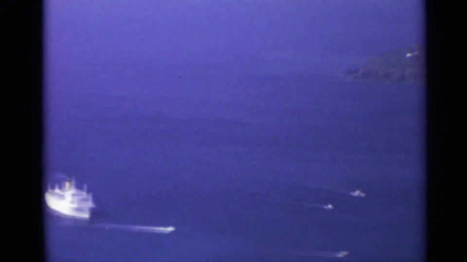 1967 U.S. Virgin Islands home-movie frame with a distant white ship, boat wakes, blue sea, and hazy rocky islands.