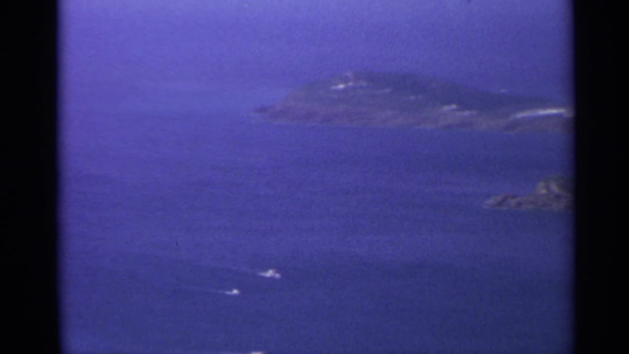 Small boats and wakes on blue water with rocky islets in the distance.