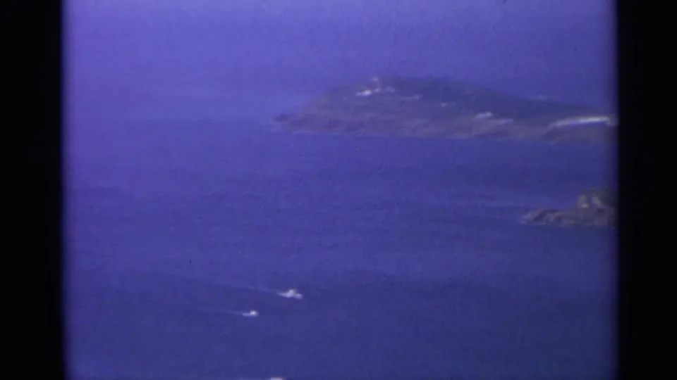 1967 U.S. Virgin Islands coastal view showing small boat wakes across blue water and low rocky islets under haze.