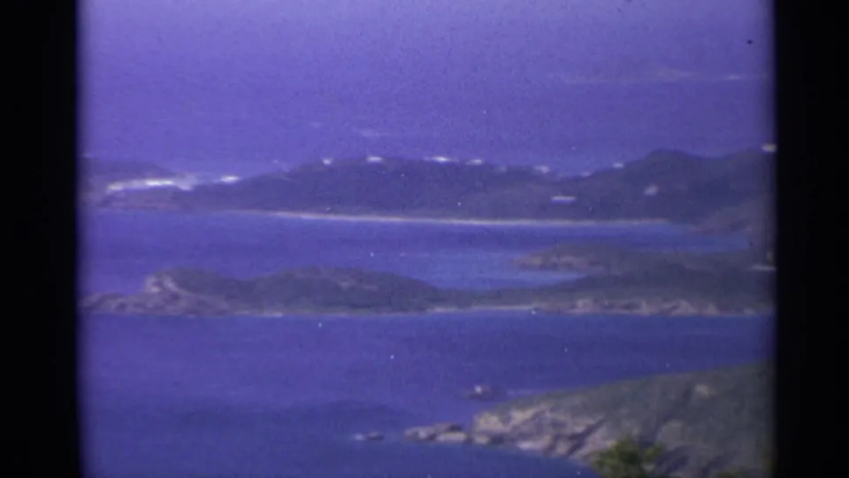 1967 U.S. Virgin Islands wide coastal frame with layered islands, blue water, white shoreline marks, and a rocky foreground point.