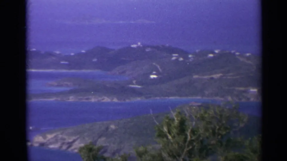 1967 U.S. Virgin Islands panorama with blue sea, green hills, scattered white buildings, and trees at the lower edge.