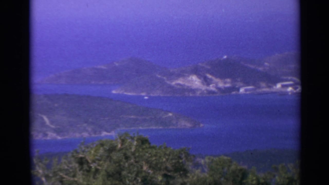 Blue ocean and hilly island shoreline with scattered pale buildings in the distance.