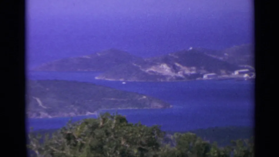 Panoramic 8mm frame of the US Virgin Islands coastline, with blue water, green hills, and small white structures along the far shore.