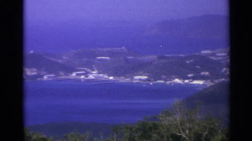 Final frame of the 8mm pan across a US Virgin Islands bay, showing distant hillside structures, blue water, and trees in the foreground.