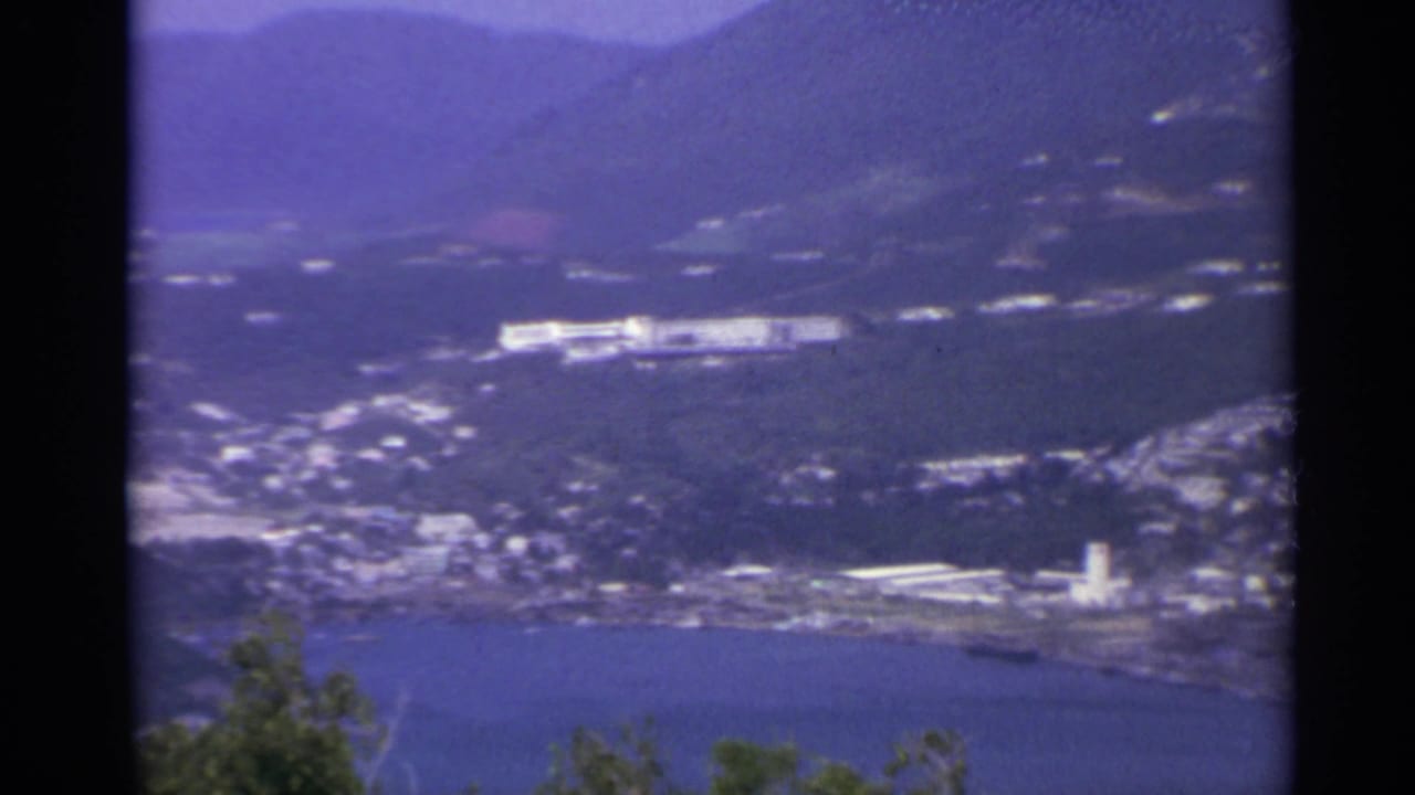 1967 US Virgin Islands home-movie view of a coastal bay, green hills, scattered white buildings, and distant mountains.