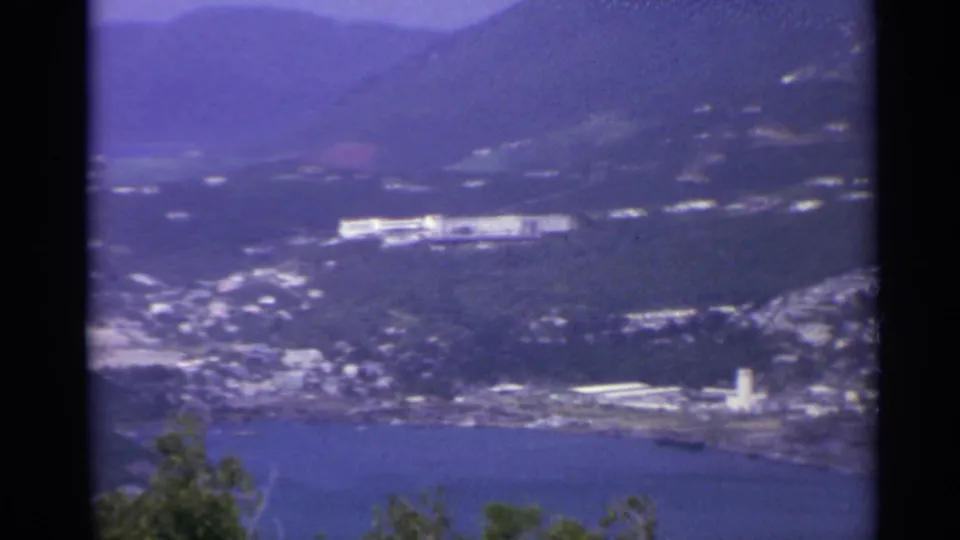 1967 US Virgin Islands home-movie view of a coastal bay, green hills, scattered white buildings, and distant mountains.