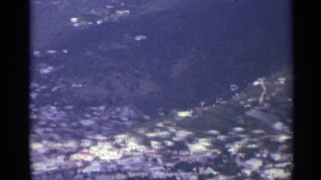 Aerial view of hillside buildings and coastline through a dark vertical frame edge.