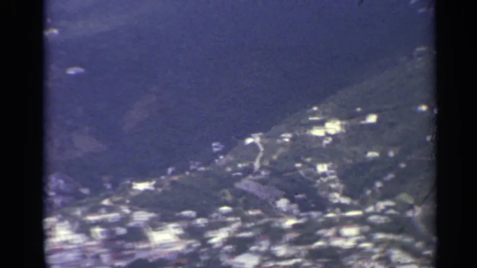 Oblique 1967 8mm aerial view of US Virgin Islands shoreline, water, hillside greenery, and scattered buildings.