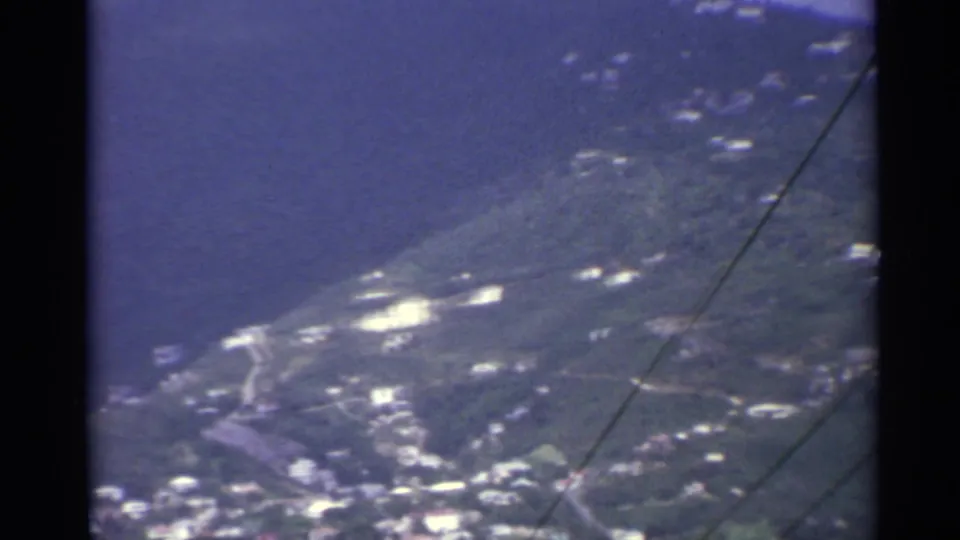 1967 US Virgin Islands aerial frame with shoreline terrain, hillside roads, bright buildings, and a diagonal line across the view.