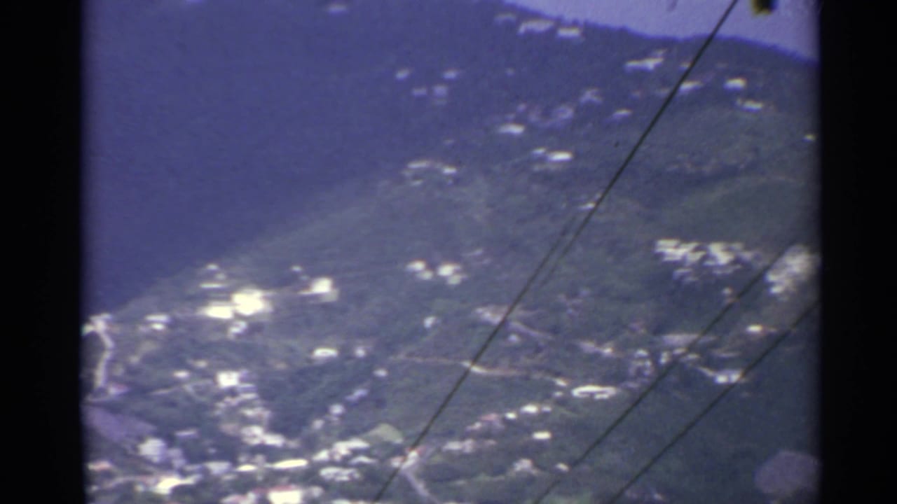 Forested hillside with scattered white buildings and diagonal utility wires in the foreground.