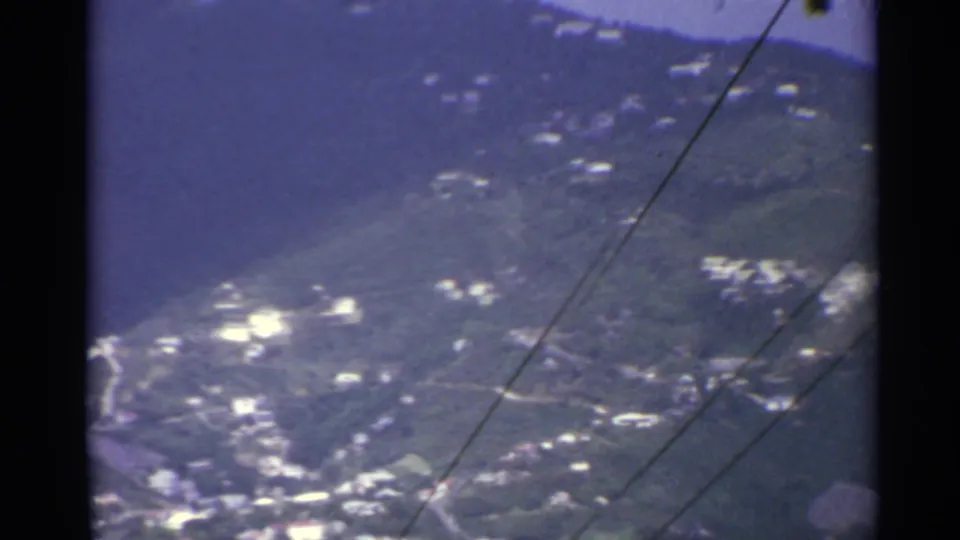1967 US Virgin Islands 8mm view of green mountains, scattered hillside buildings, and foreground utility wires from an elevated vantage.