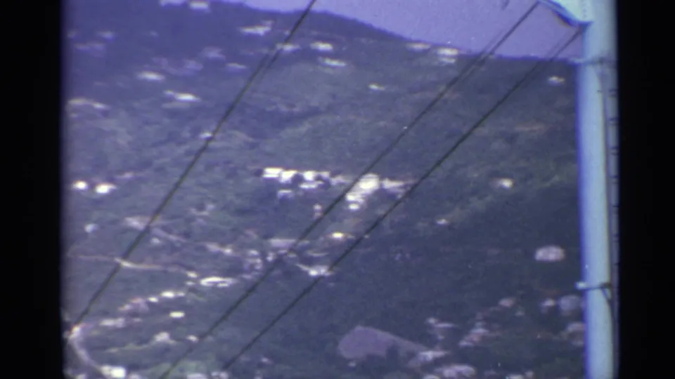 Elevated 8mm view in the US Virgin Islands showing a green hillside, white buildings, diagonal lines, and part of a utility pole.