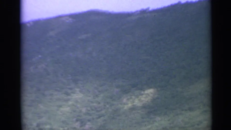 1967 home-movie aerial frame of a green US Virgin Islands hillside, with soft focus and visible small-gauge film edges.