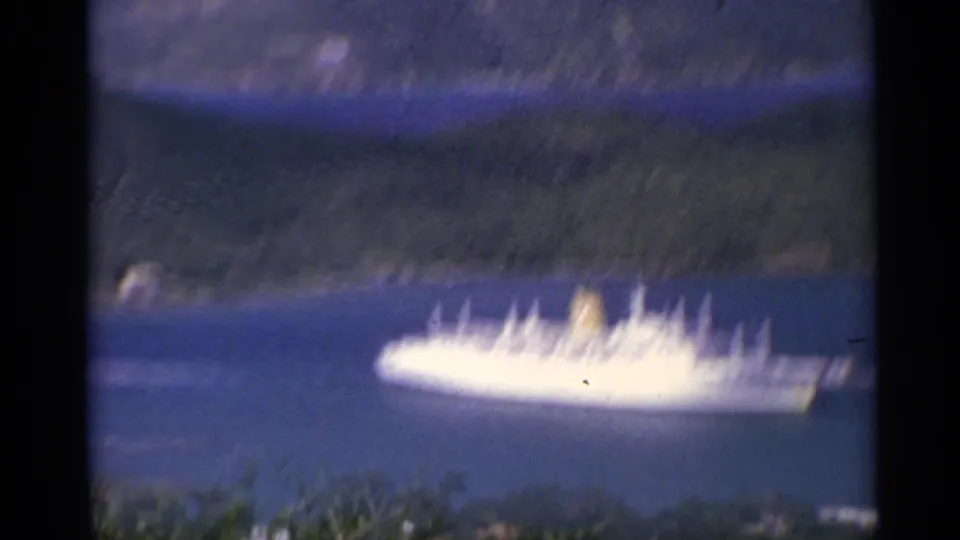 1967 8mm travel frame showing a white cruise ship on deep blue water with green mountain slopes behind it.