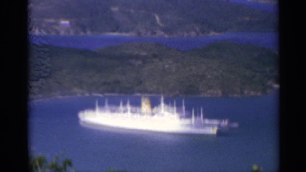 White passenger ship in a blue bay with wooded hills behind.