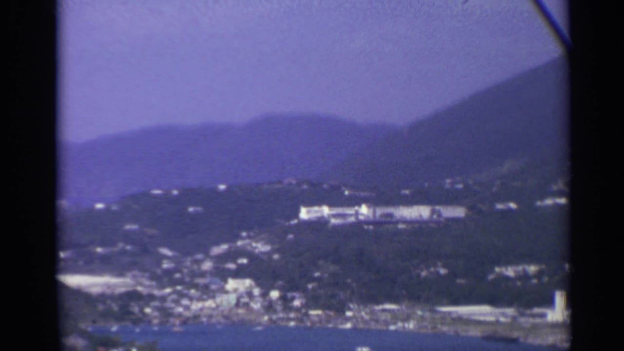 Hazy coastal town below purple hills with harbor water at the bottom edge.