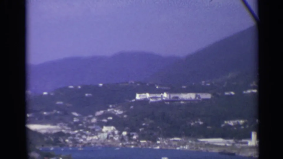 1967 US Virgin Islands home-movie view of a coastal town and hills above a harbor, softened by 8mm grain and color fading.