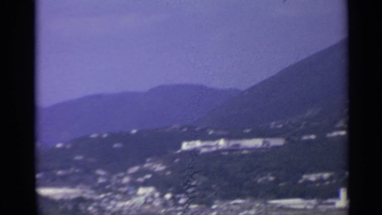 Hillside coastline with a bright waterfront building and town below.