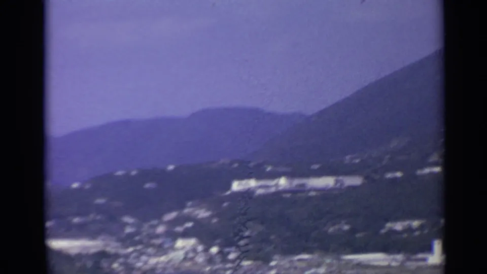 Elevated 1967 US Virgin Islands view across a hillside coast, with a bright waterfront structure and harbor town below.