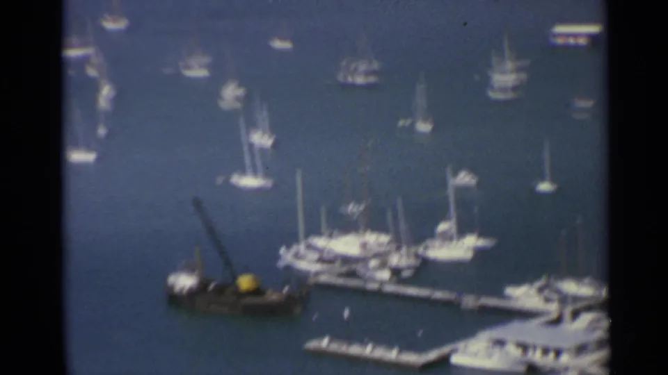 1967 US Virgin Islands harbor view with anchored sailboats, marina docks, yachts, and a small dark boat in blue water.