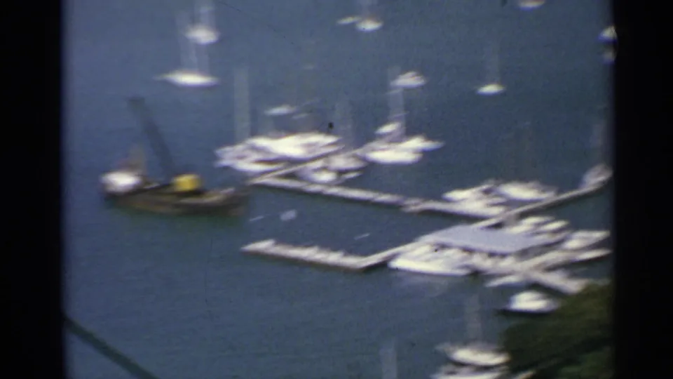 Elevated 1967 US Virgin Islands marina view showing piers, sailboats, yachts, and a dark workboat on blue harbor water.