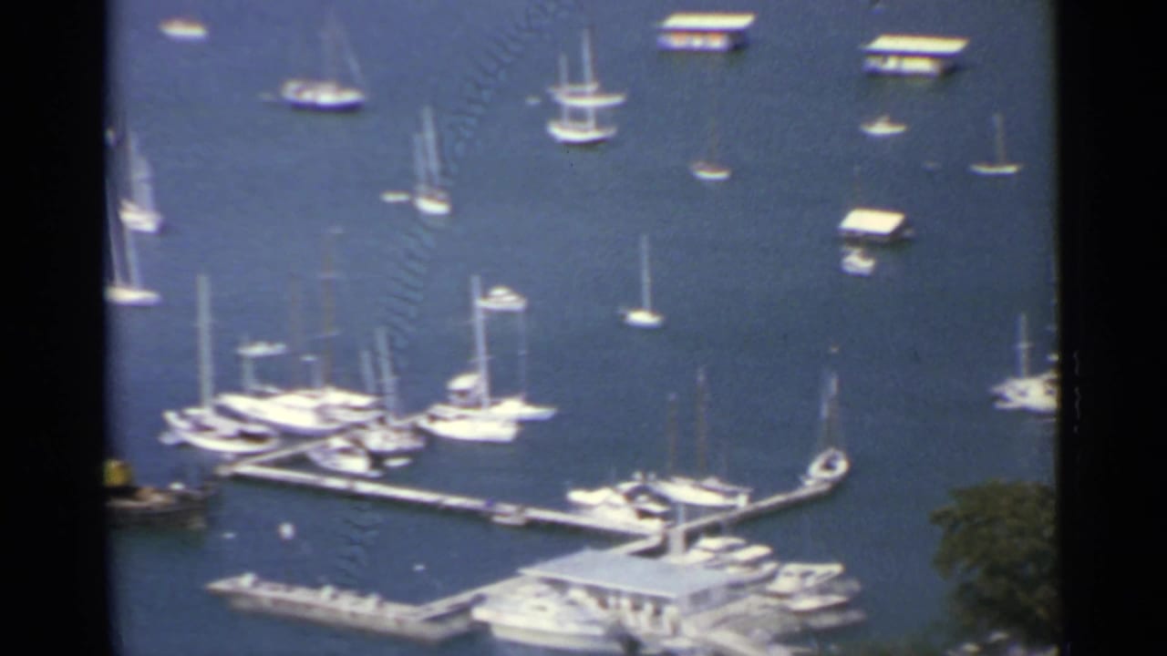 1967 US Virgin Islands home-movie frame showing white sailboats, docks, and anchored boats in a tropical harbor.