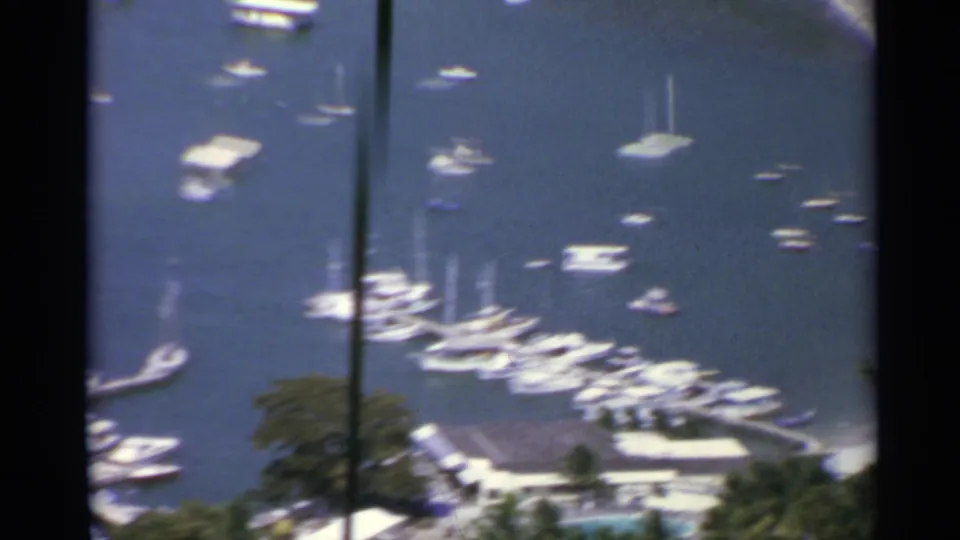 Soft 8mm frame from a 1967 US Virgin Islands harbor pan, with clustered boats, docks, trees, and a shoreline roof.