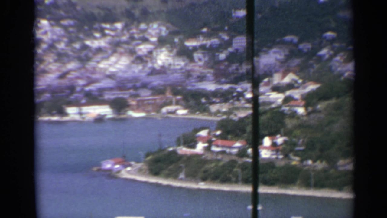 1967 US Virgin Islands harbor view showing a developed hillside, waterfront buildings, trees, and blue bay water.