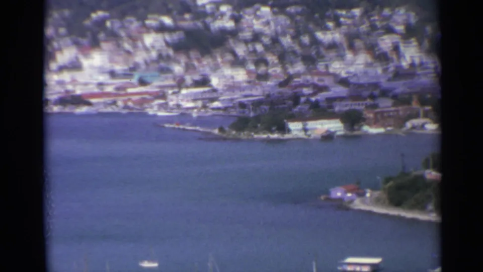 Wide 1967 8mm view across a US Virgin Islands bay with boats, shoreline buildings, and a dense hillside settlement.