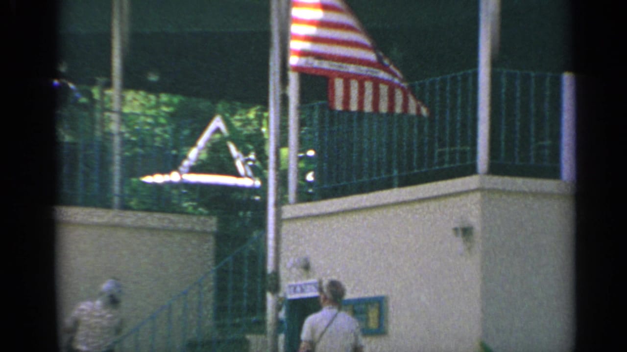 1967 8mm US Virgin Islands travel frame showing an American flag, tramway station facade, ticket booth, and visitors below.