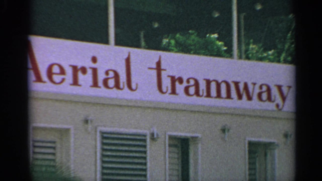 Red aerial tramway sign on a pale building facade with vents and windows.