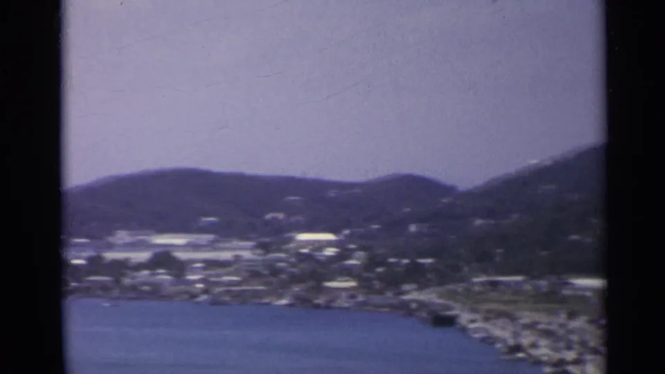 1967 8mm view over a harbor-side settlement, water, and hills in the US Virgin Islands.