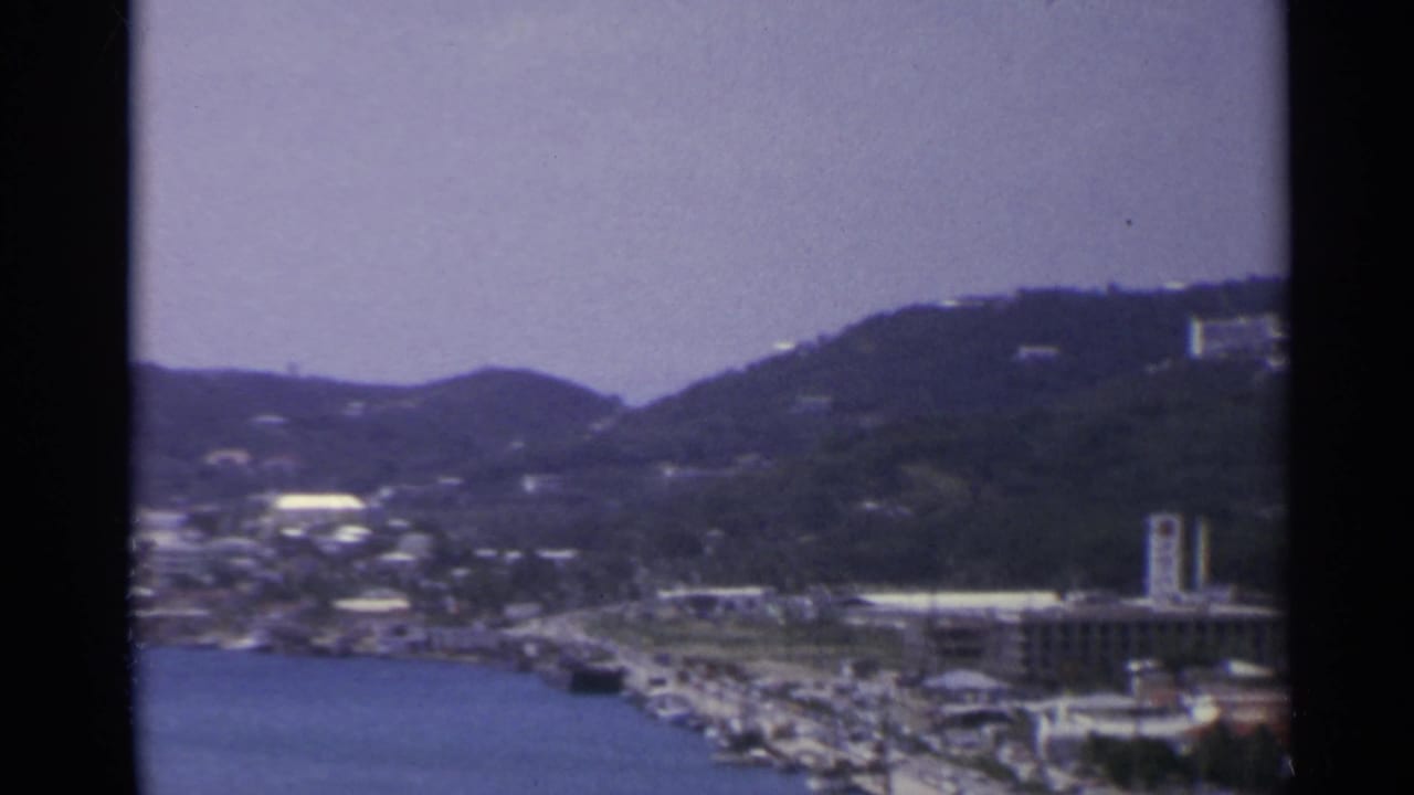 1967 U.S. Virgin Islands 8mm view across a bay toward a hillside town with clustered buildings and waterfront activity.