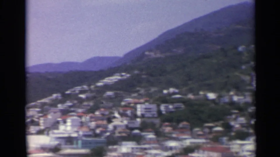1967 U.S. Virgin Islands 8mm frame of hillside roads and scattered buildings rising above a coastal town.