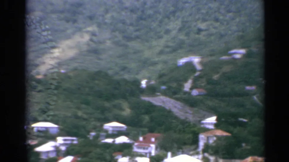 1967 US Virgin Islands home-movie frame showing a winding road, scattered homes and dense greenery on sloped terrain.