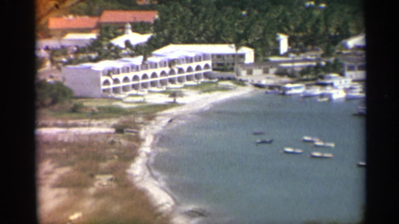 Coastal beach with a white arched waterfront building and small boats offshore.