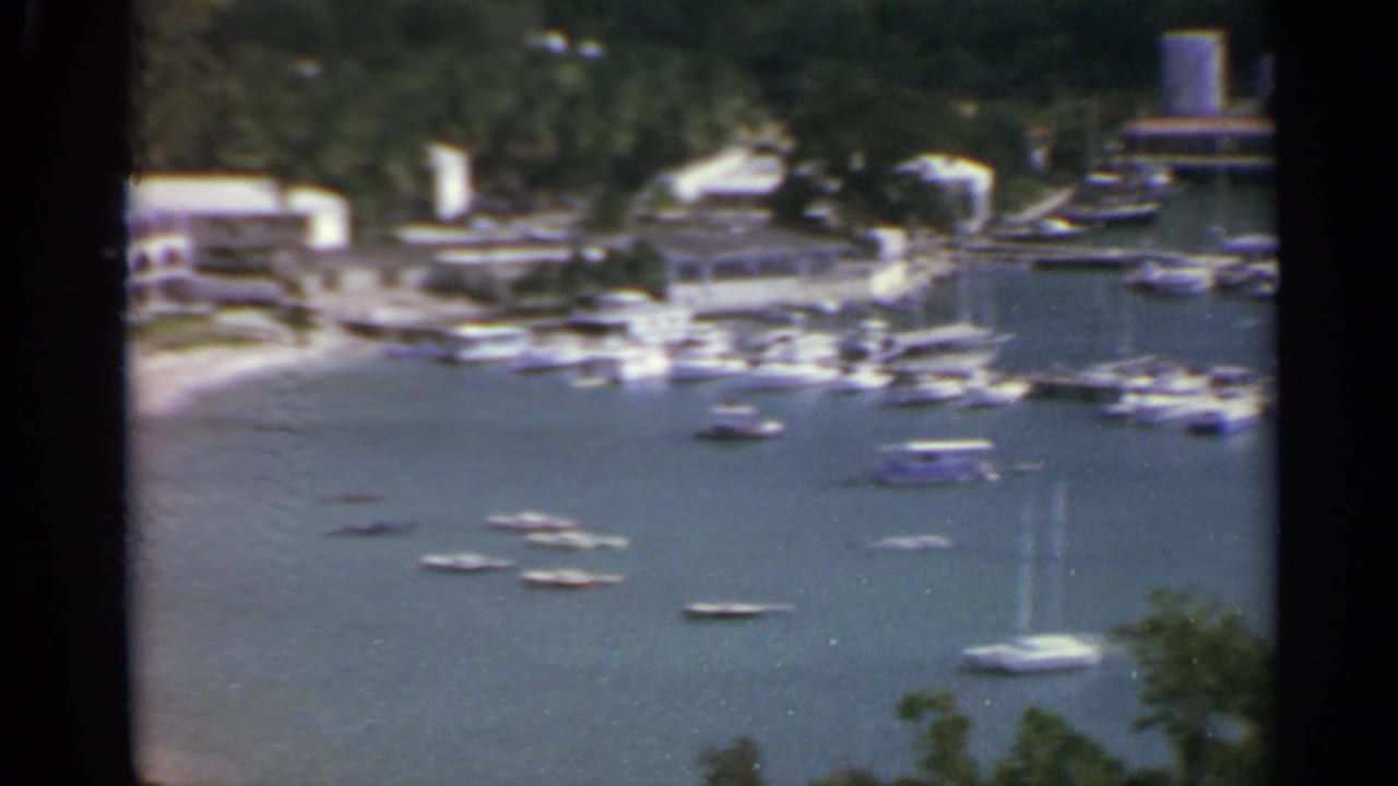 Harbor with many small boats, hillside buildings, and a water tank in the distance.