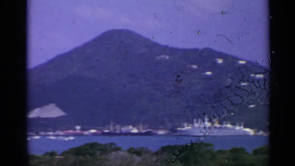 1967 US Virgin Islands view of a distant cruise ship at the base of a green hillside across the harbor.