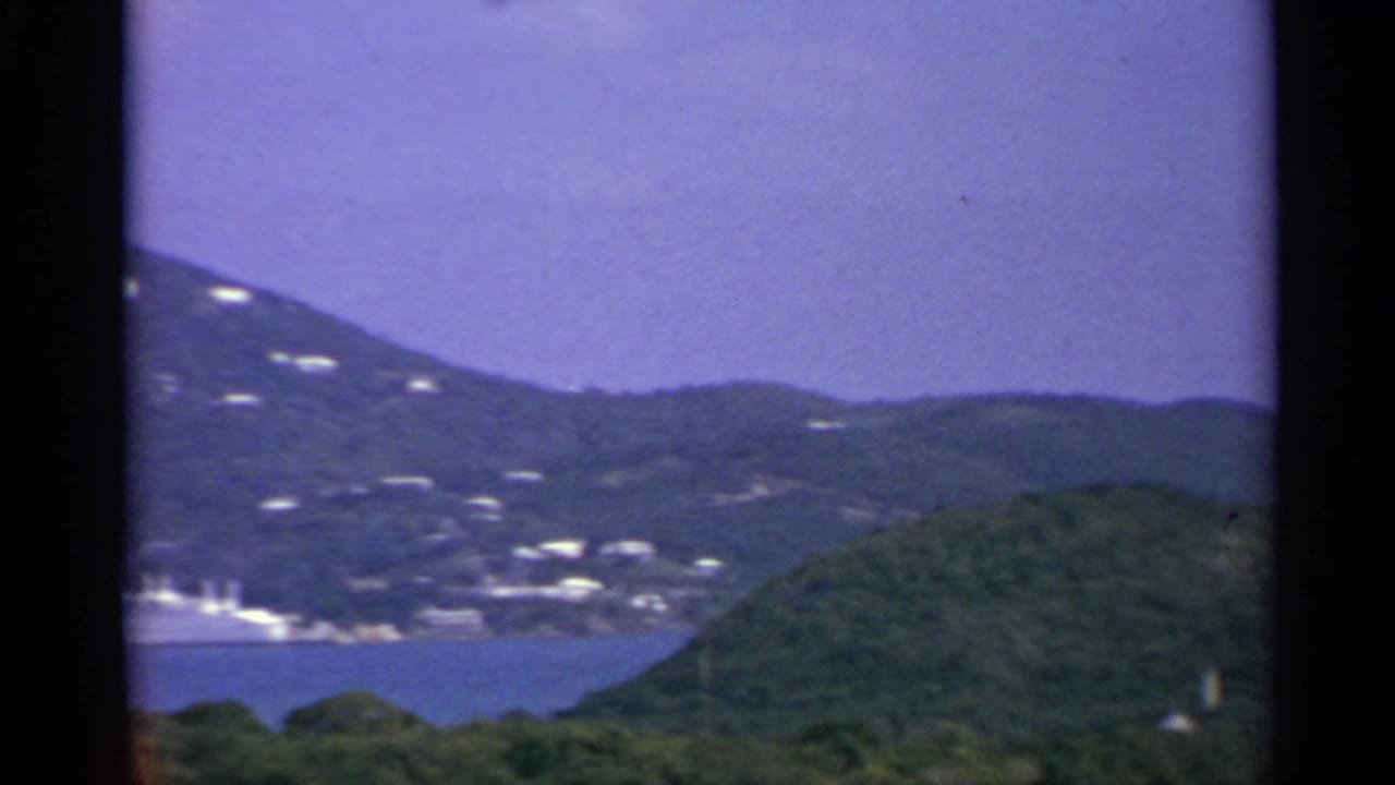 Coastal hills with white buildings, blue water, and purple-tinted sky.