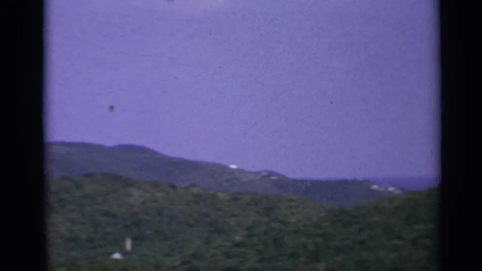US Virgin Islands landscape frame showing a wooded foreground ridge, distant mountain slopes, and purple color-shifted sky.