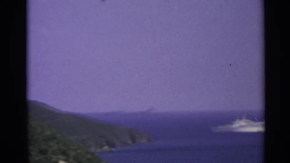1967 8mm US Virgin Islands view of a distant white cruise ship moving across blue water near green coastal inlets.