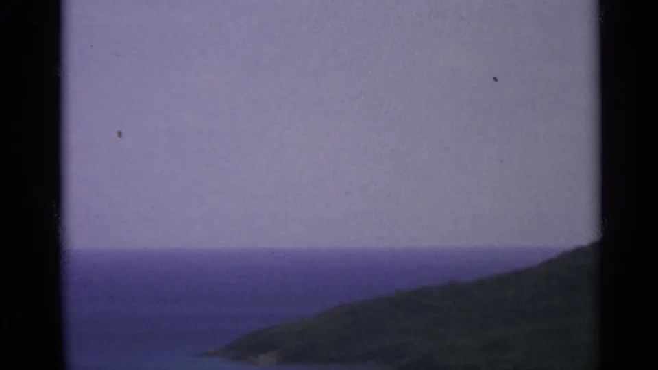 US Virgin Islands coastal view on 8mm film, showing open sea, hazy horizon, and a green inlet hillside after the ship has passed.