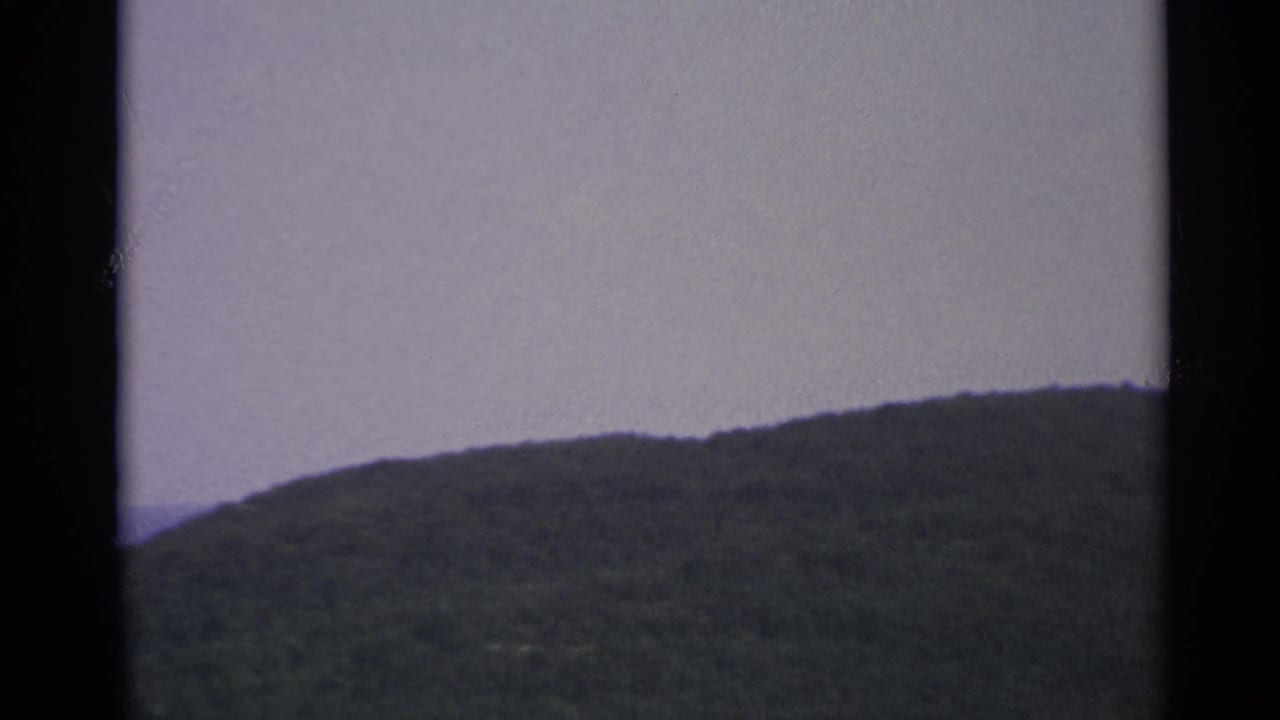 Green ridge fills the right side with pale sky above and dark contact-sheet bars around it.